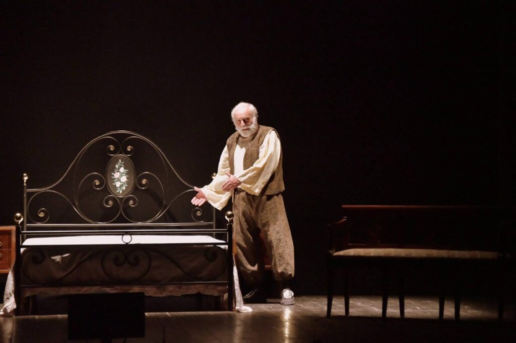 Un interprete accanto al letto di scena de «Il caso Migliorini»